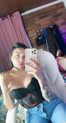 Kaunis tyttö poseeraa puhelimessaan korsetissa ja farkuissa