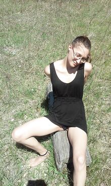 Nuori silmälasipäinen kaunotar istuu tukin päällä ja näyttää jalkojaan